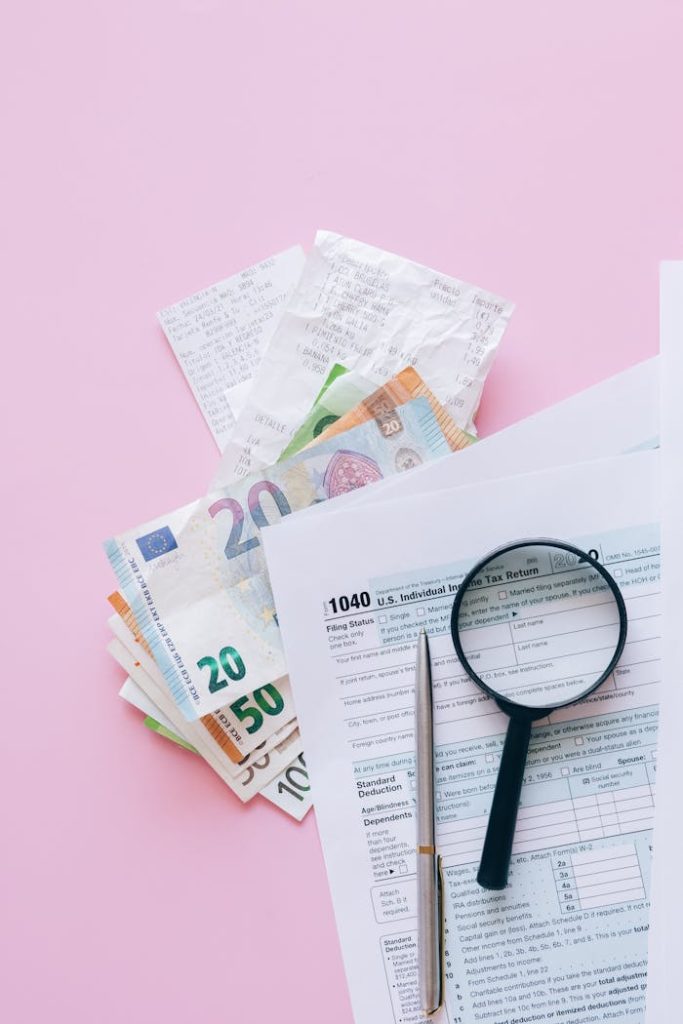 A collection of financial papers, including euro notes, tax return forms, and receipts on a pink surface.